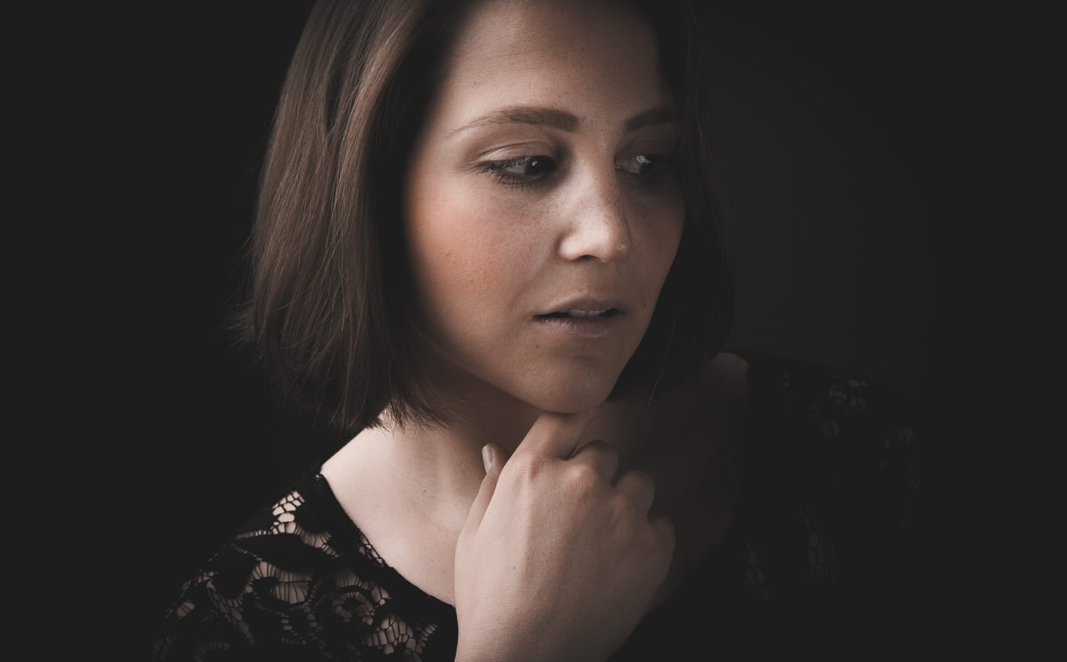Frau mit schulterlangem Haar, die nachdenklich zur Seite schaut, vor dunklem Hintergrund.