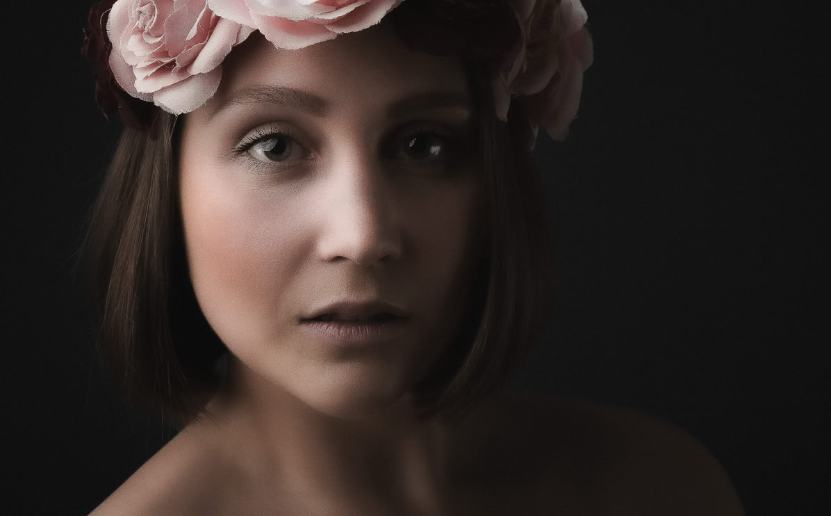Frau mit Blumenkranz im Haar vor dunklem Hintergrund.