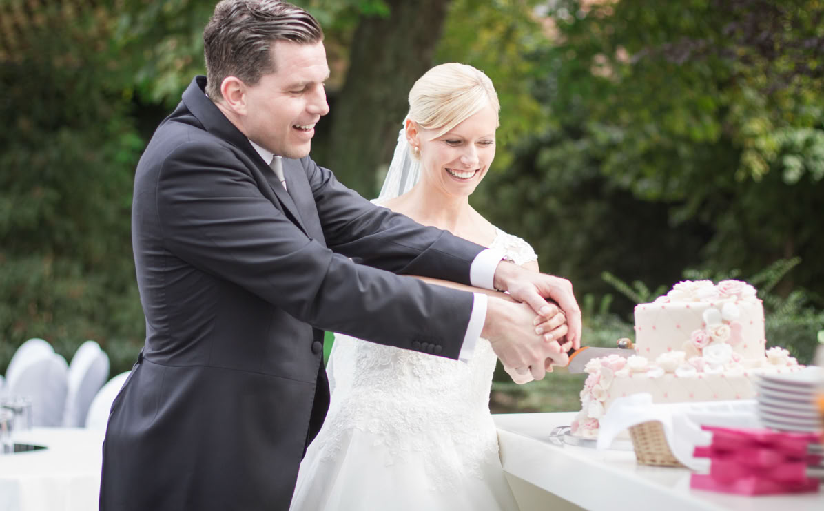 Ein Paar in formeller Kleidung schneidet gemeinsam eine Hochzeitstorte an.