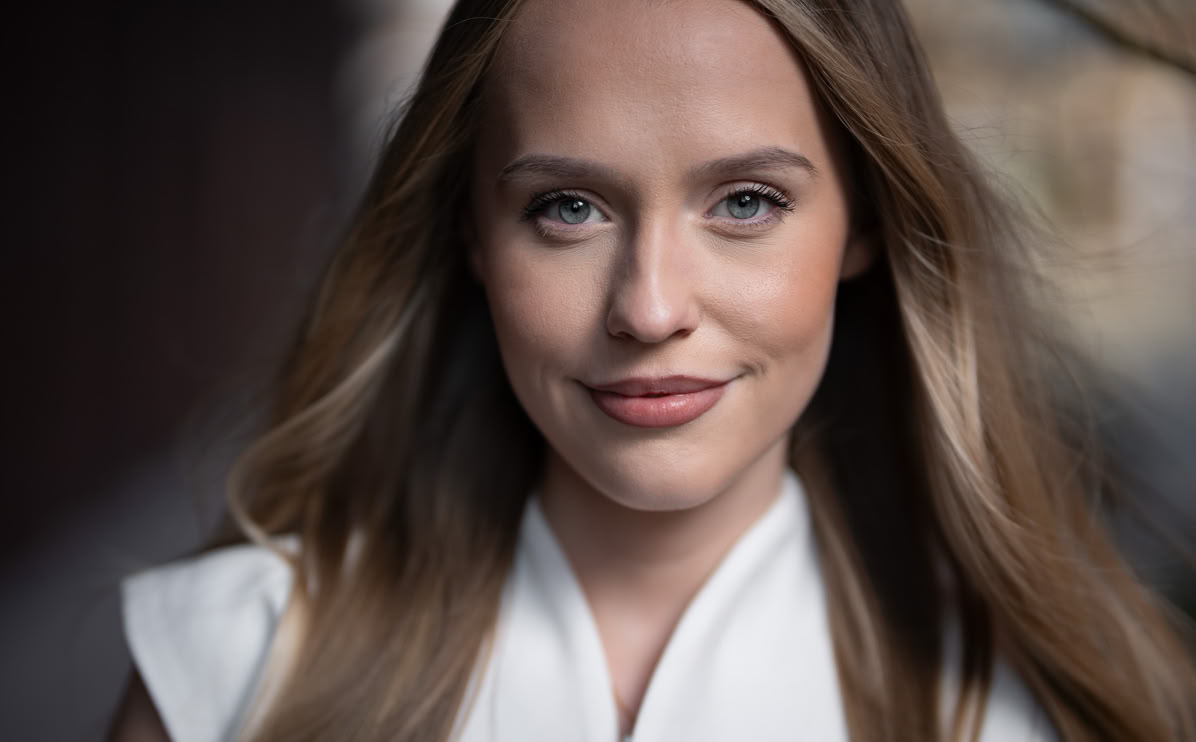 Eine Frau mit langen, blonden Haaren und einem weißen Oberteil lächelt in die Kamera.