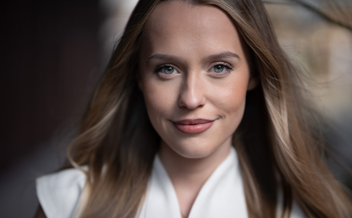 Eine Frau mit langen, blonden Haaren und einem weißen Oberteil lächelt in die Kamera.